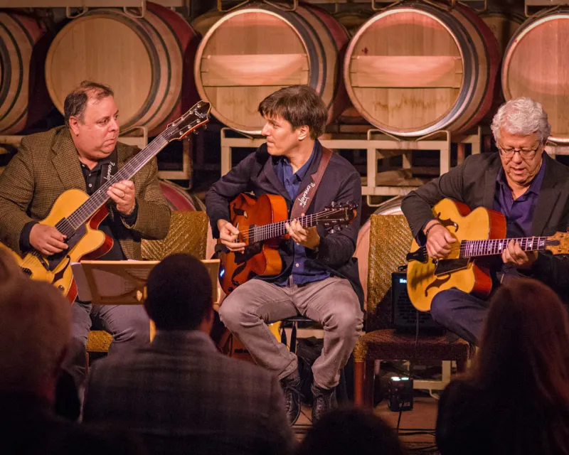 Three men playing Benedetto guitars at a winery
