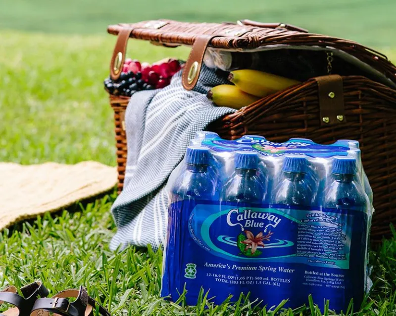 An eight-pack of Callaway Blue water beside a picnic basket on a green lawn