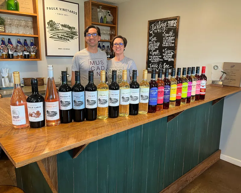 Chris and Jorjanne Paulk stand behind a bar with a display of wines in front.