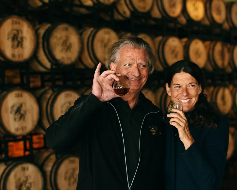 Richland Rum owners pose with glasses of rum in front of barrels