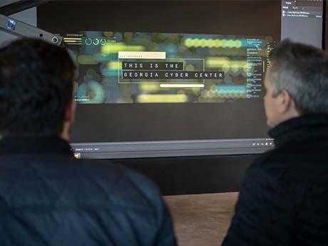 Georgia Cyber Center two people look at a screen that says "This is the Georgia Cyber Center"