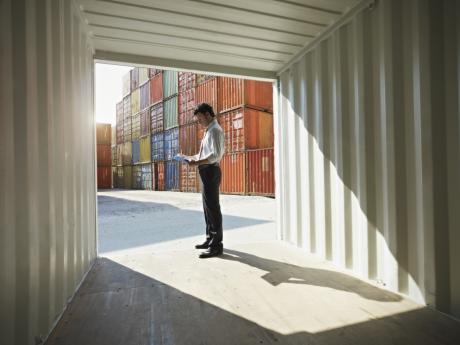 A person in business attire stands inside an empty shipping container in Georgia looking at a paper. Behind them are stacks of additional shipping containers.