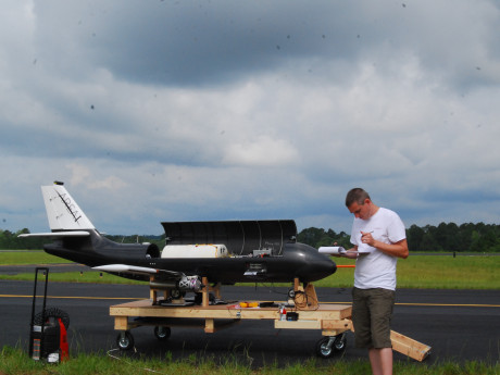 A person in casual clothes stands on an air field in Georgia next to a plane and takes notes. 