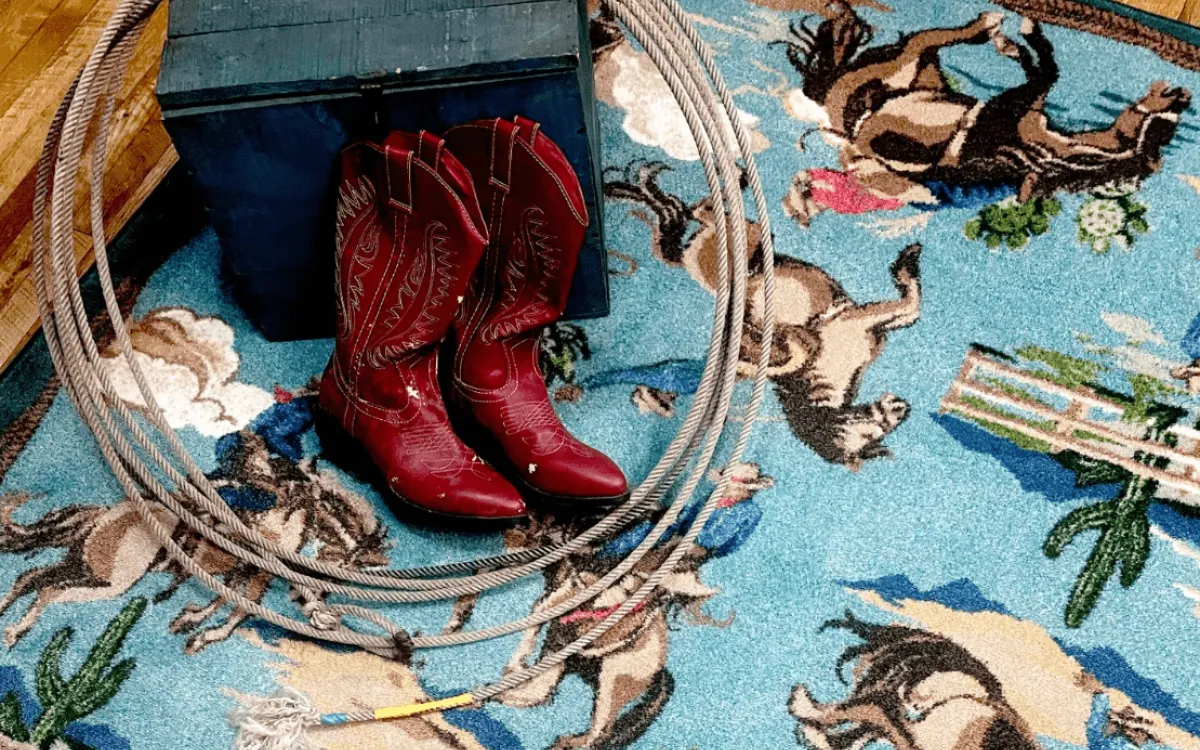 Red cowboy boots and a rope on a rug with horses and cowboys