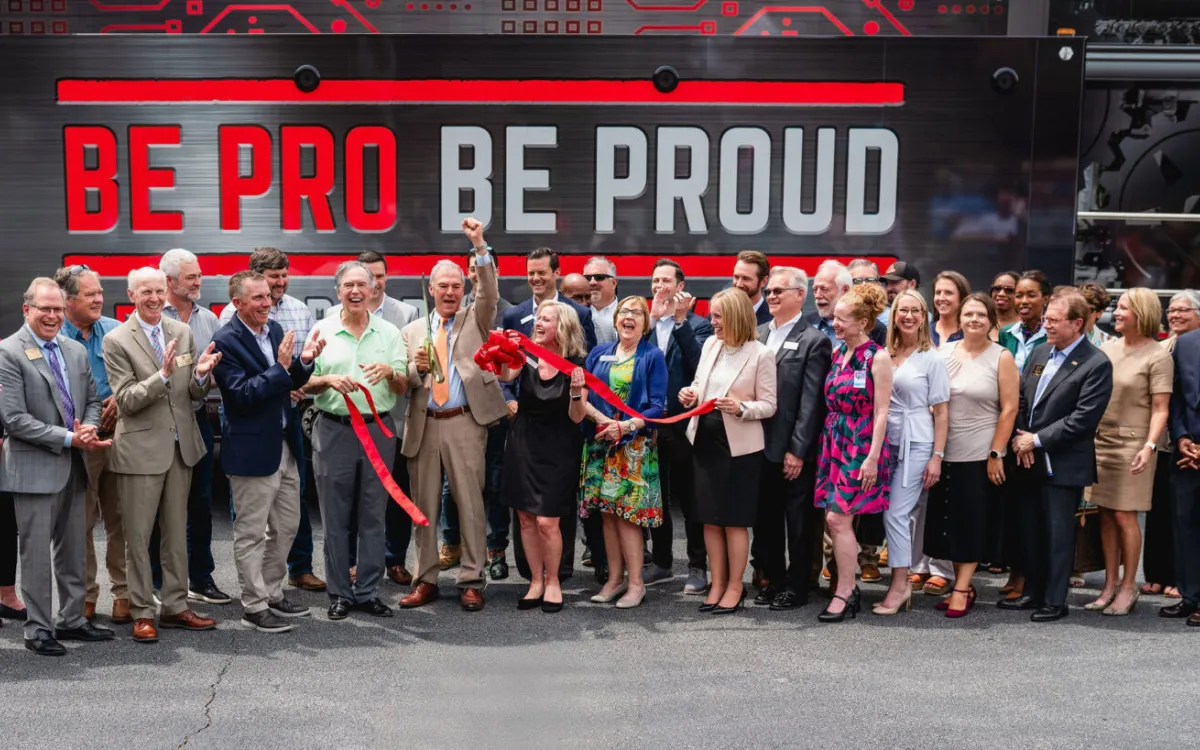 Group cut a red ribbon in front of a background sign that reads, "Be Pro Be Proud"
