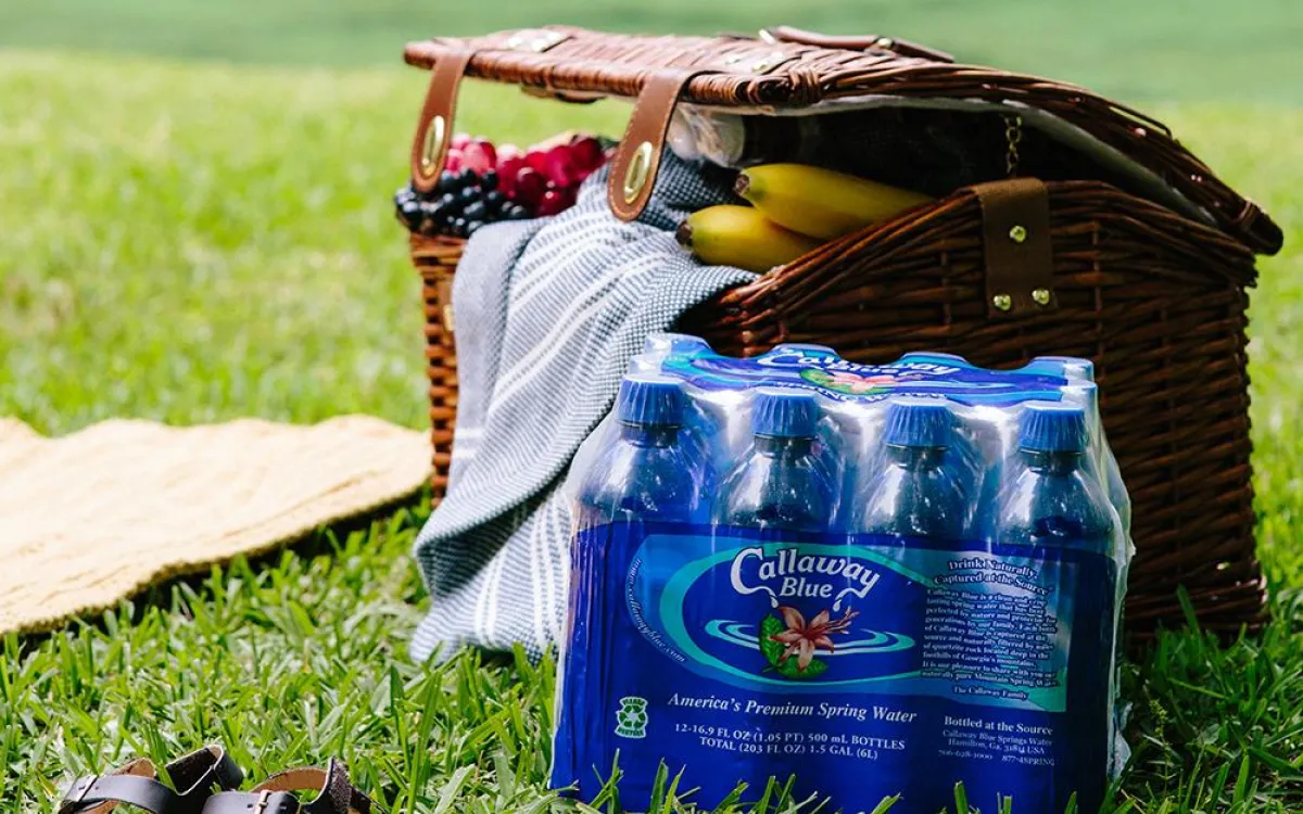 An eight-pack of Callaway Blue water beside a picnic basket on a green lawn