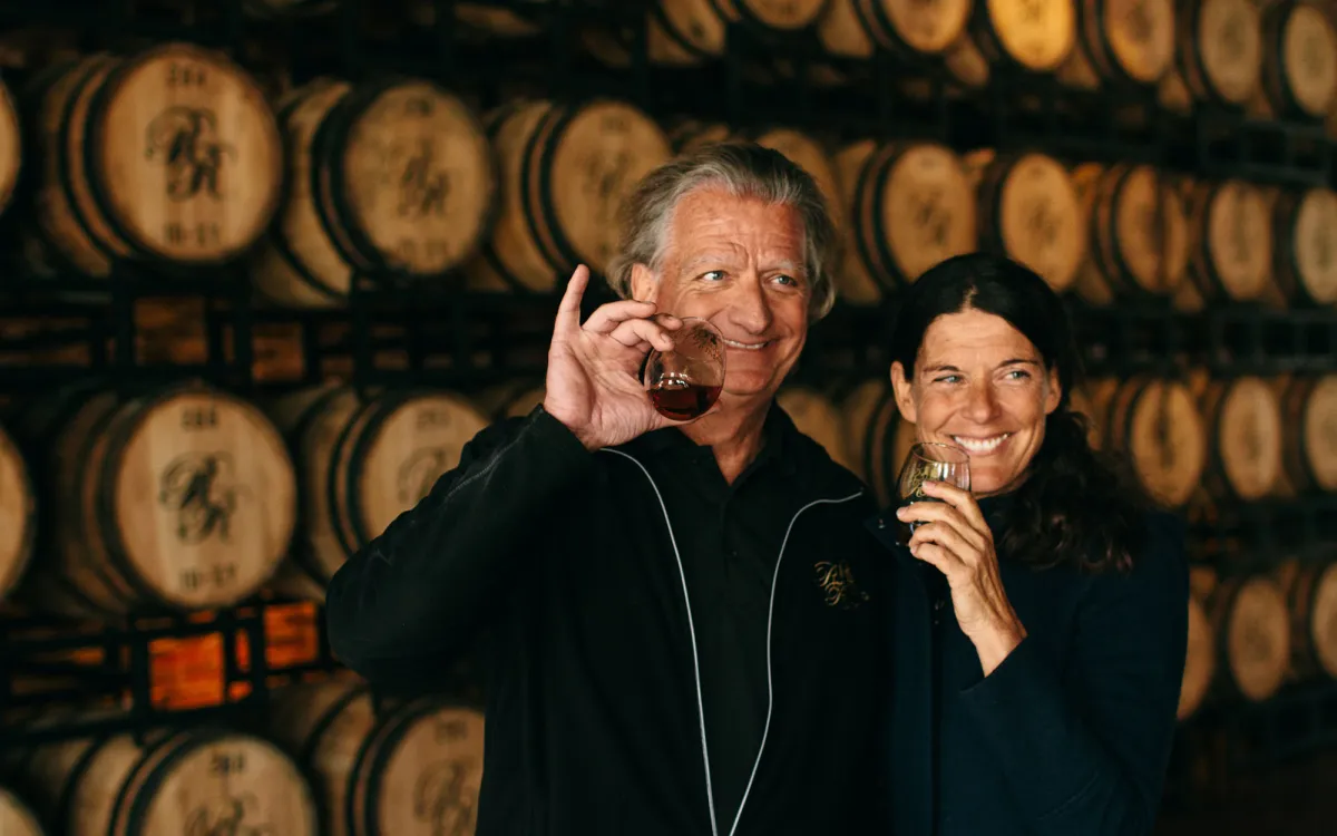Richland Rum owners pose with glasses of rum in front of barrels