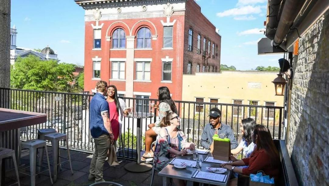 People sit and laugh on a rooftop patio in downtown Valdosta large red-brick building in the background