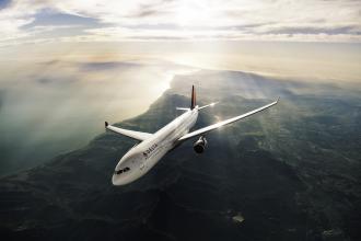 A Delta airplane flies through the air with the sun shining in the background