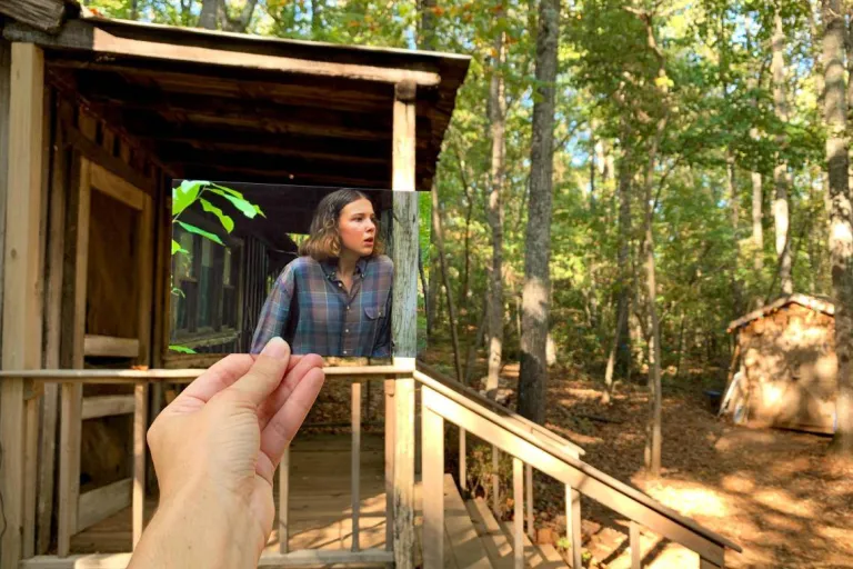 Person holds a photo of Eleven in front of the actual location of Hopper's Cabin